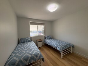 A small, single-room accommodation with two single beds, a window with a view, and a ceiling light. - Pumicestone Chase U8 Jetty, Pool & Views (Caloundra)