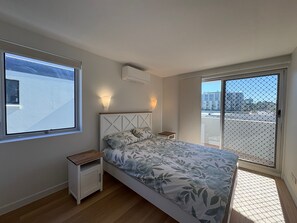 A bedroom with a bed, a nightstand, a wall-mounted air conditioner, a window, and a sliding glass door leading to an outdoor area. - Pumicestone Chase U8 Jetty, Pool & Views (Caloundra)