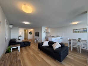 A modern living room with a black sofa, a wooden coffee table, and a kitchen area in the background. - Pumicestone Chase U8 Jetty, Pool & Views (Caloundra)