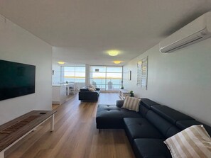 A modern living room with a black sofa, a wooden bench, and a TV mounted on the wall. - Pumicestone Chase U8 Jetty, Pool & Views (Caloundra)