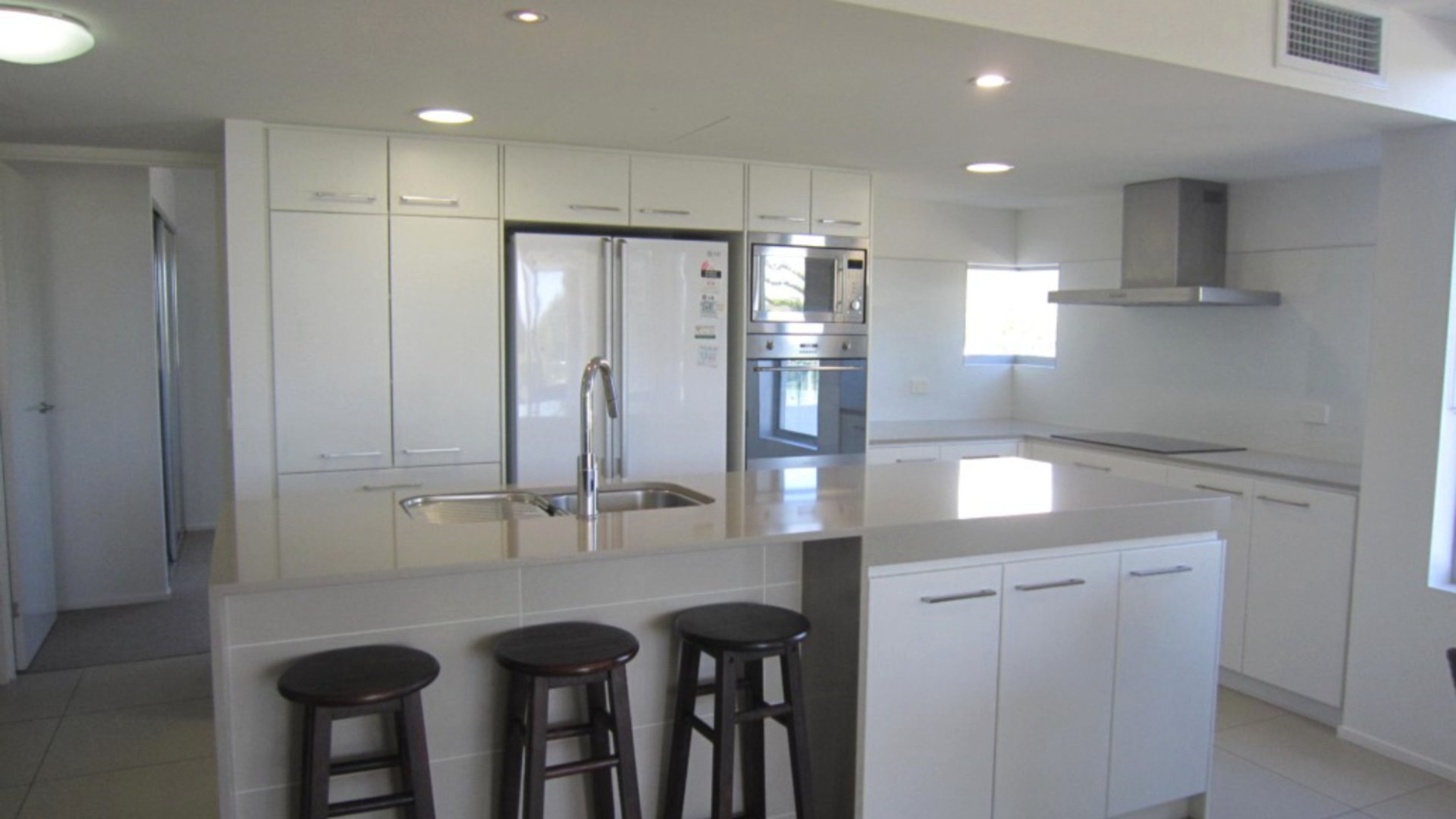 A modern kitchen with white cabinetry, stainless steel appliances, and a central island with stools.
