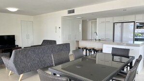 Une cuisine moderne avec des meubles blancs, un réfrigérateur encastré et un coin repas comprenant une table en verre et des chaises en osier.