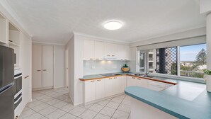 A modern kitchen with white cabinetry, a blue countertop, and a view of the outdoors through a window.