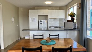 A kitchen with white cabinets, a refrigerator, a sink, and a window with a view. - Summervale - Central Caloundra Apt, Pool & Beach (Caloundra)
