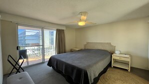 Una habitación de hotel con una cama, una silla, una mesita de noche y un ventilador de techo, con vistas al exterior a través de una puerta corredera.
