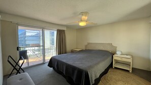 A hotel room with a bed, a chair, a nightstand, a bedside table, a ceiling fan, and a view of the outside through a sliding door. - Summervale - Central Caloundra Apt, Pool & Beach (Caloundra)