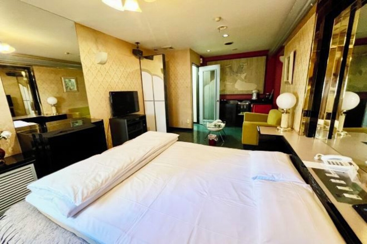 A hotel room with a large bed, a desk with a telephone, a mirror, and a small seating area.