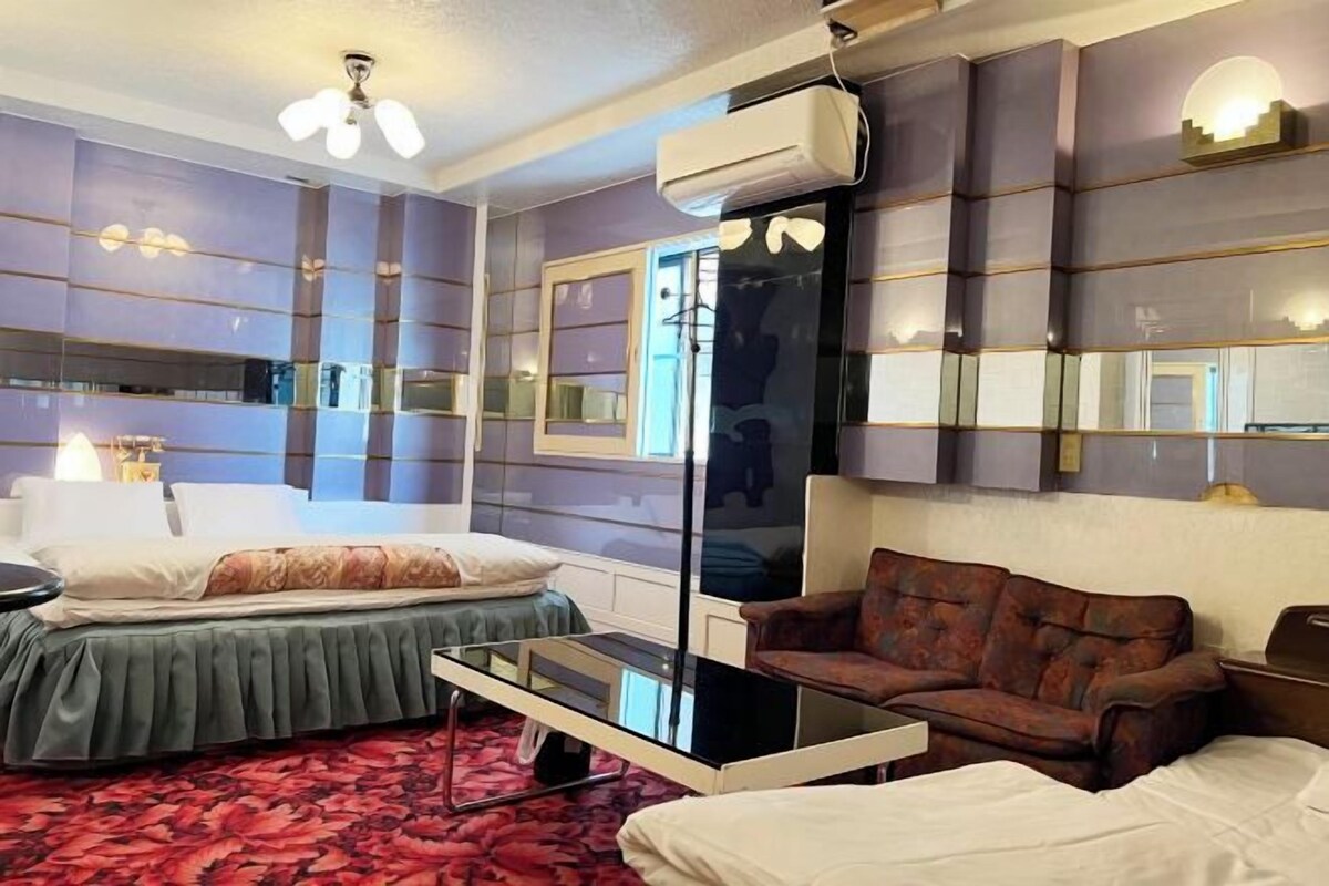A hotel room with a bed, a sofa, a glass coffee table, and a large mirror.