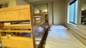 Une chambre avec un lit superposé et une fenêtre, des lits superposés en bois et un lit simple avec une literie blanche.