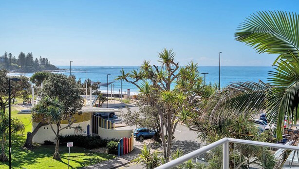 A coastal view with a beach, palm trees, and a building with a curved roof. - Panoramic Ocean Views, Family Unit (Kings Beach)