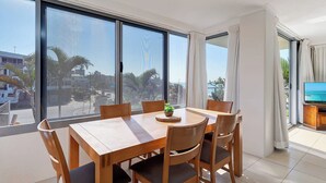A dining area with a large table and chairs, a television, and a view of palm trees and buildings. - Panoramic Ocean Views, Family Unit (Kings Beach)