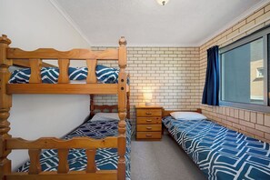 A room with two bunk beds, a bedside table with a lamp, and a window with curtains.
