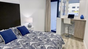 A hotel room with a bed, a desk, and a view of the outside. - Grand Pacific U10 | Waterfront Views Direct Pool Access (Caloundra)