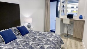 A hotel room with a bed, a desk, and a view of the outside. - Grand Pacific U10 | Waterfront Views Direct Pool Access (Caloundra)