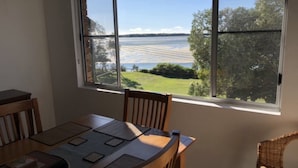 A dining area with a table and chairs, a window with a view of a body of water and greenery.