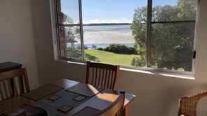 Un comedor con una mesa y sillas, una ventana con vista a un cuerpo de agua y vegetación.