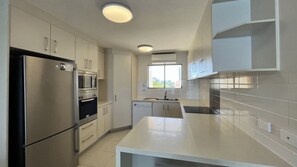 Una cocina moderna con electrodomésticos de acero inoxidable, armarios blancos y un amplio ventanal que proporciona luz natural.