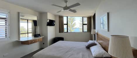 A hotel room with a bed, a ceiling fan, a TV, a window with a view, and a bedside lamp.