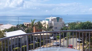 Zona residencial con vista al mar, con edificios modernos, coches estacionados y barandilla de balcón.