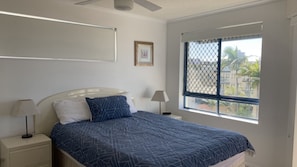A bedroom with a bed, two bedside tables, a ceiling fan, a window with a view, and a framed picture on the wall. - Sahara Sands U4-Kings Beach Escape (Kings Beach)