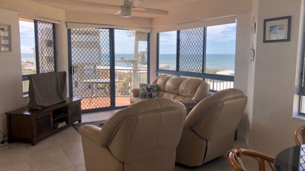 A living room with a television, leather recliner chairs, and a balcony with a view of the ocean.