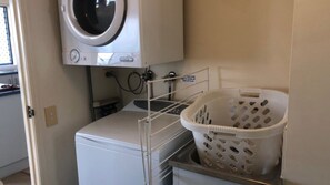 A laundry area with a washing machine, a drying rack, and a laundry basket. - Sahara Sands U4-Kings Beach Escape (Kings Beach)
