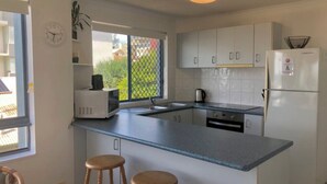 Cocina compacta con microondas, lavamanos y refrigerador. Hay dos taburetes y una ventana con vista a follaje.