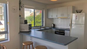 A compact kitchen with a microwave, sink, and refrigerator. There are two stools and a window with a view of greenery. - Sahara Sands U4-Kings Beach Escape (Kings Beach)