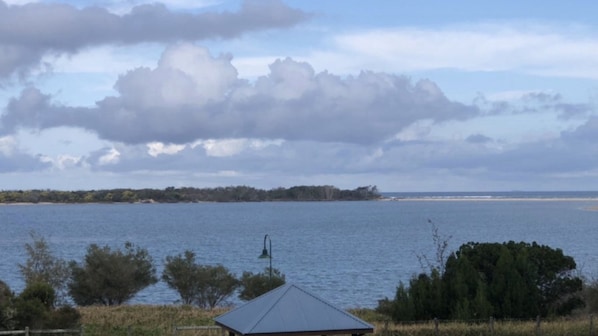 A coastal landscape with a body of water, a distant shoreline, and a small structure with a triangular roof.