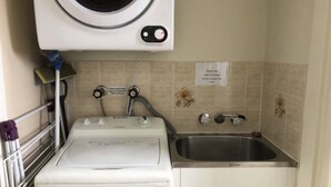 Zona de lavandería compacta con lavadora, un lavabo y un letrero que indica retirar la ropa antes de usar la secadora.