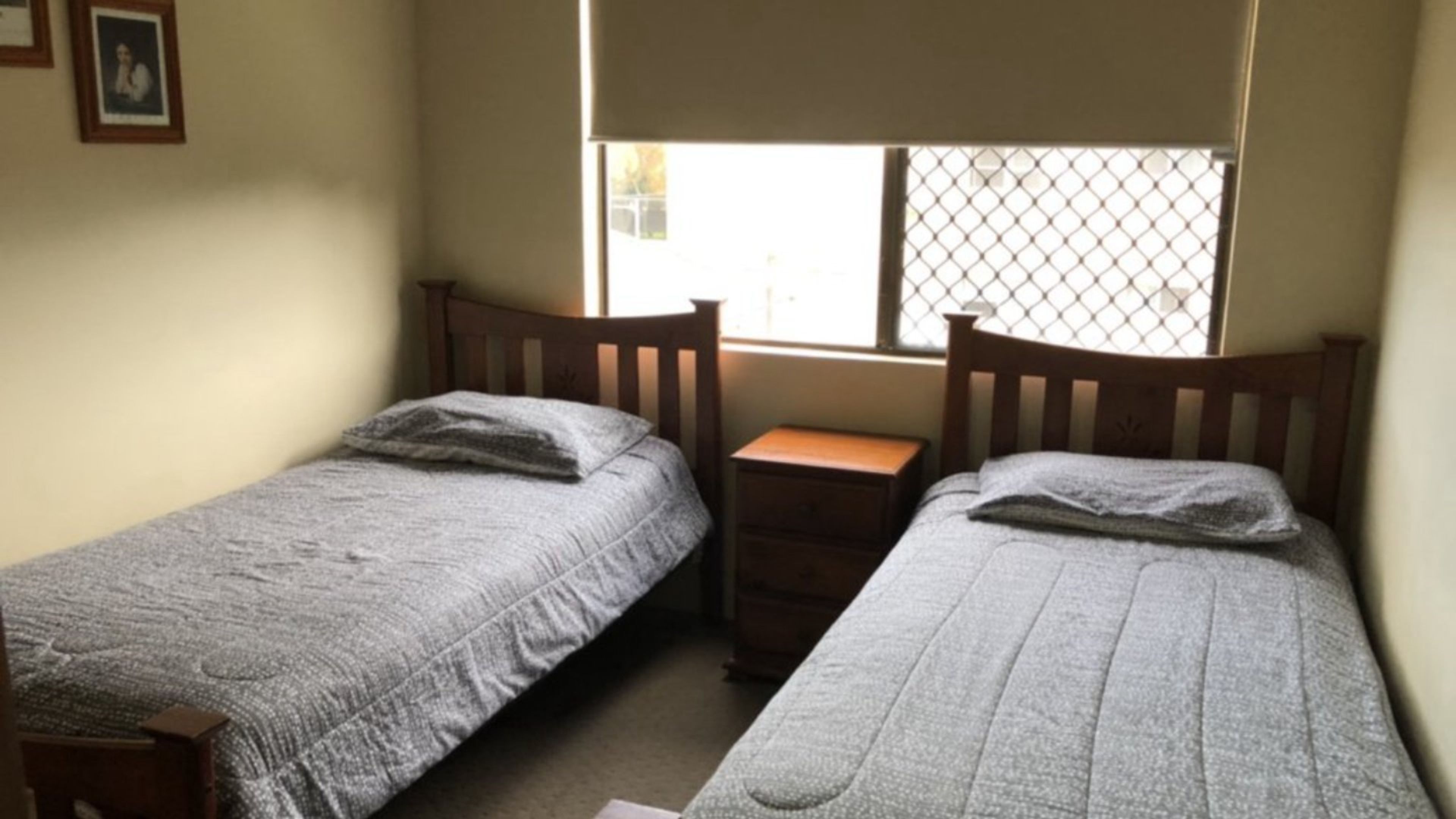 A small room with two single beds, a wooden nightstand, and a window with a metal screen.