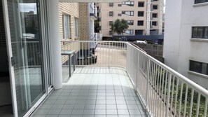 Een balkon met betegelde vloer, metalen hekwerk en uitzicht op een parkeerplaats en gebouwen op de achtergrond.