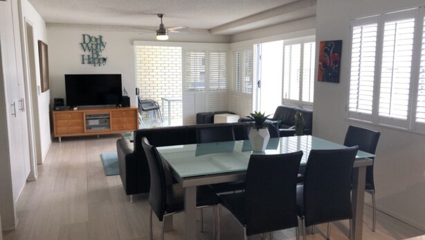A modern dining area with a glass-top table and black chairs, a flat-screen TV on a wooden cabinet, and a brick wall with a motivational quote. - Spinnaker Seas Walk To Kings Beach | Ocean Views | Pool (Kings Beach)