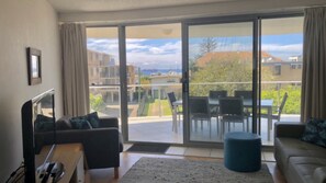 Een woonkamer met een bank, een salontafel en een televisie. Er is een balkon met een tafel en stoelen.