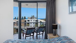 A balcony with two wicker chairs, a lamp, and a bed with a patterned bedspread. - Centrepoint 27 | Ocean Views Walk To Bulcock Beach (Caloundra)