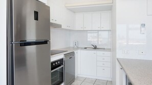 A modern kitchen with stainless steel appliances, white cabinetry, and a tiled backsplash. - Centrepoint 27 | Ocean Views Walk To Bulcock Beach (Caloundra)