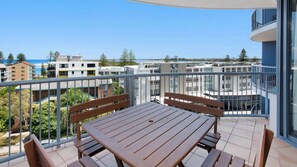 A balcony with a table and chairs, overlooking a residential area with buildings and a clear sky. - Centrepoint 27 | Ocean Views Walk To Bulcock Beach (Caloundra)
