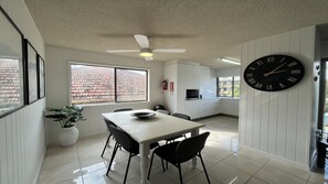 A modern kitchen with white cabinetry, a dining table with chairs, a ceiling fan, and a large wall clock.