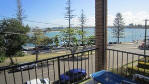 A balcony with a view of a parking lot, a body of water, and a distant city skyline. - Balamara U3 Water Views, Walk to Bulcock Beach (Caloundra)