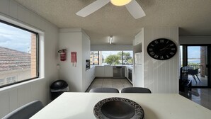 Une cuisine moderne avec une grande fenêtre, un coin repas doté d’une table blanche et une horloge noire accrochée au mur.