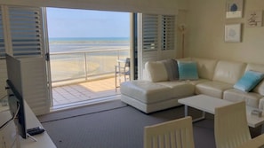 A living room with a sofa, a coffee table, a TV, and a balcony with a view of the beach. - The Moorings 906 Golden Beach Waterfront Views (Golden Beach)