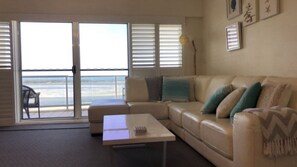 A living room with a sofa, a coffee table, and a view of the ocean through large windows. - The Moorings 906 Golden Beach Waterfront Views (Golden Beach)