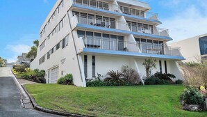 Un edificio de varios pisos con techo plano, balcones y un césped bien cuidado.