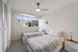 Un dormitorio con dos camas, ventilador de techo, ventana con vistas y mesita de noche con lámpara.