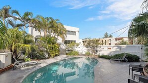 A swimming pool with a curved edge, surrounded by palm trees and a white building. - Wickham Point - Kings Beach With Ocean Views (Kings Beach)