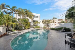 A swimming pool with a curved edge, surrounded by palm trees and a white building.