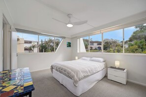 A bedroom with a bed, nightstands, a ceiling fan, and large windows.