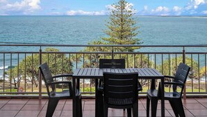 A balcony with a table and chairs overlooking a body of water and a tree. - Wickham Point - Kings Beach With Ocean Views (Kings Beach)