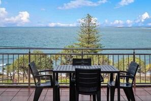 A balcony with a table and chairs overlooking a body of water and a tree.