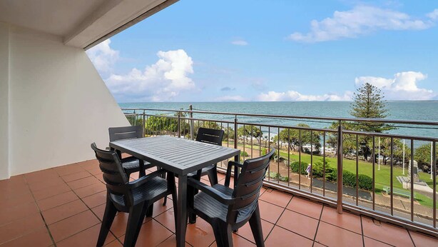 A balcony with a table and chairs, overlooking a coastal view with a clear sky. - Wickham Point - Kings Beach With Ocean Views (Kings Beach)